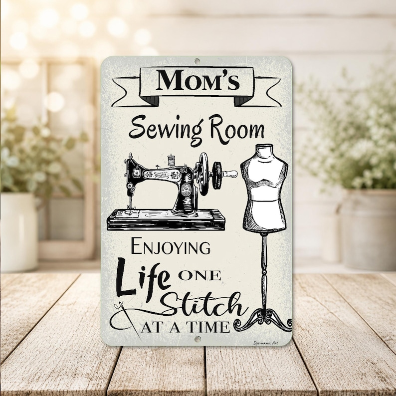 May include: A rectangular metal sign with the words "Mom's Sewing Room" above a sewing machine and dress form illustration. The sign also includes the phrase "Enjoying Life One Stitch At A Time."