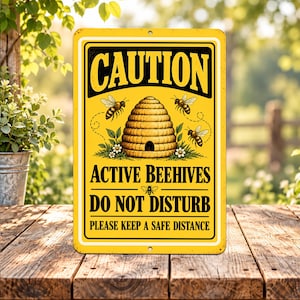 May include: A rectangular yellow metal sign with black text and graphics. The sign reads CAUTION ACTIVE BEEHIVES DO NOT DISTURB PLEASE KEEP A SAFE DISTANCE. It features a central illustration of a beehive, three bees, and small white flowers.