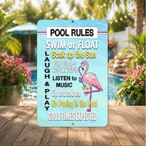 May include: A rectangular metal sign with a light blue background and the words "POOL RULES" at the top. The sign features a pink flamingo with a cocktail and the text "SWIM or FLOAT, Soak up the Sun, LAUGH, LISTEN to MUSIC, PLAY, GOOD TIMES EXPECTED."