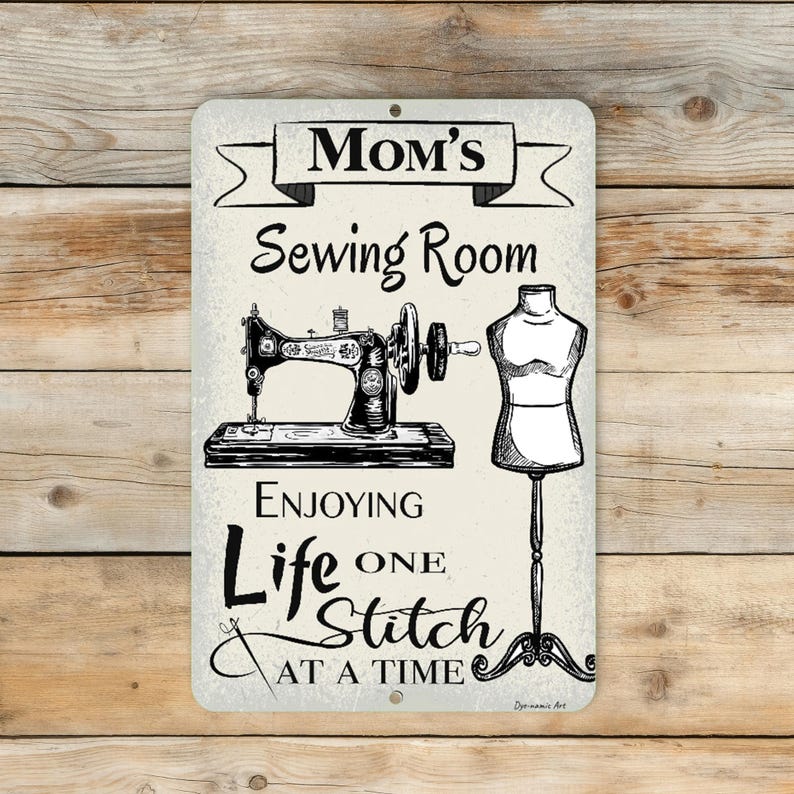 May include: A rectangular metal sign with the words "Mom's Sewing Room" above a sewing machine and dress form illustration. The sign also includes the text "Enjoying Life One Stitch at a Time."