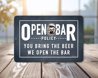 May include: A rectangular sign with the words "OPEN BAR POLICY" in white capital letters. The sign also reads "YOU BRING THE BEER WE OPEN THE BAR". A beer mug graphic is in the center of the sign.