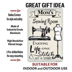 May include: A rectangular metal sign with the text "Mom's Sewing Room" and an illustration of a vintage sewing machine and dress form. The sign also includes the text "Enjoying Life One Stitch at a Time" and is suitable for indoor and outdoor use.