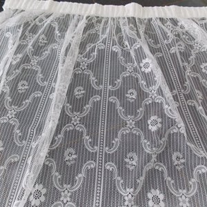 May include: White lace curtain panel with a delicate floral pattern. The lace is sheer and has a gathered top edge.