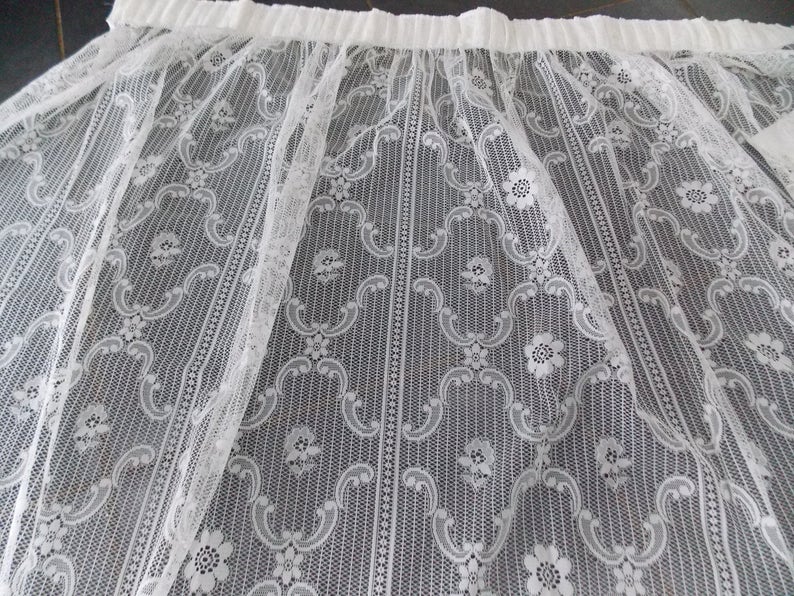 May include: White lace curtain panel with a delicate floral pattern. The lace is sheer and has a gathered top edge.
