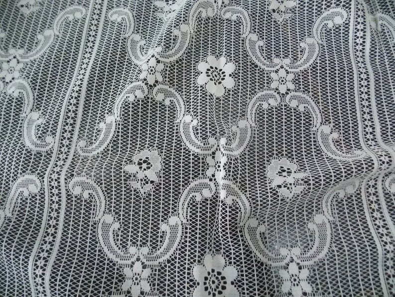 May include: White lace fabric with a delicate floral pattern. The fabric is woven in a fine mesh and has a soft, flowing texture.