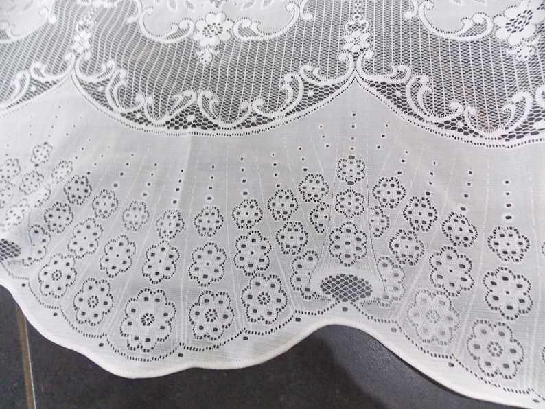 May include: White lace tablecloth with a scalloped edge and a floral pattern. The lace is delicate and intricate, with small flowers and leaves.