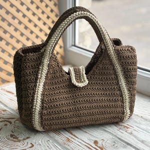 May include: A brown crocheted tote bag with cream colored trim. The bag has a single handle and a flap closure.