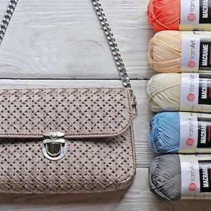 Puede incluir: Un bolso tejido marrón con una correa de cadena plateada y un cierre plateado. El bolso está al lado de cinco ovillos de hilo de diferentes colores: naranja, amarillo, crema, azul y gris. Los ovillos de hilo tienen etiquetas que dicen "YarnArt Macrame".