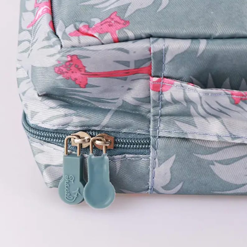 May include: Close-up of a zipper on a grey travel bag with a tropical print. The zipper pulls are blue and have the word "Travel" printed on them.