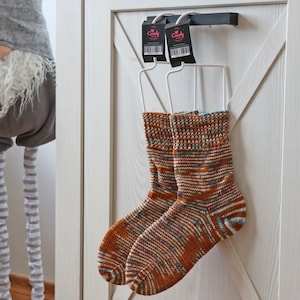 May include: Two pairs of colourful knitted socks hanging on a white hanger with the word "Candy" printed on the tags. The socks are a mix of brown, orange, blue, and white.