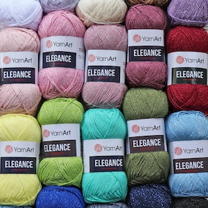 May include: Assortment of YarnArt Elegance yarn skeins in various colors, including pink, green, blue, and red. Each skein features a label with the brand name and the yarn's name, "Elegance".