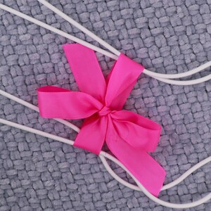 May include: White wire hangers with a pink bow tied in the center. The hangers are on a gray textured background.
