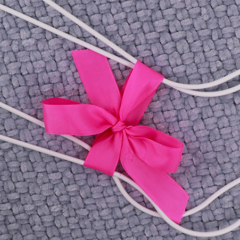 May include: White wire hangers with a pink bow tied in the center. The hangers are on a gray textured background.
