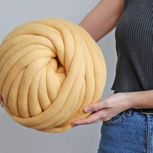 K&ouml;nnte beinhalten: Ein gro&szlig;er, runder Ball aus gelbem Garn, gehalten von einer Person. Das Garn ist dick und scheint aus einem weichen, gestrickten Material zu bestehen. Der Ball wird von einer Person gehalten, was seine Gr&ouml;&szlig;e und Textur zeigt. Ideal f&uuml;r Bastelprojekte.