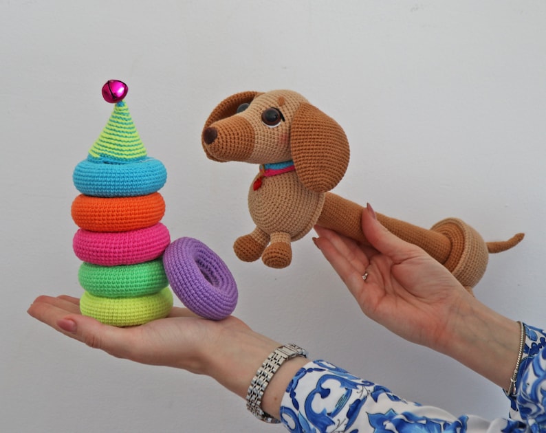 May include: A crocheted dachshund toy with a bell on its head, and a colorful stacking ring toy.