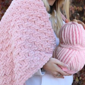 K&ouml;nnte beinhalten: Eine rosa Garnkugel und eine rosa gestrickte Decke. Das Garn ist weich und flauschig, und die Decke ist mit einem dicken Strickmuster gearbeitet.