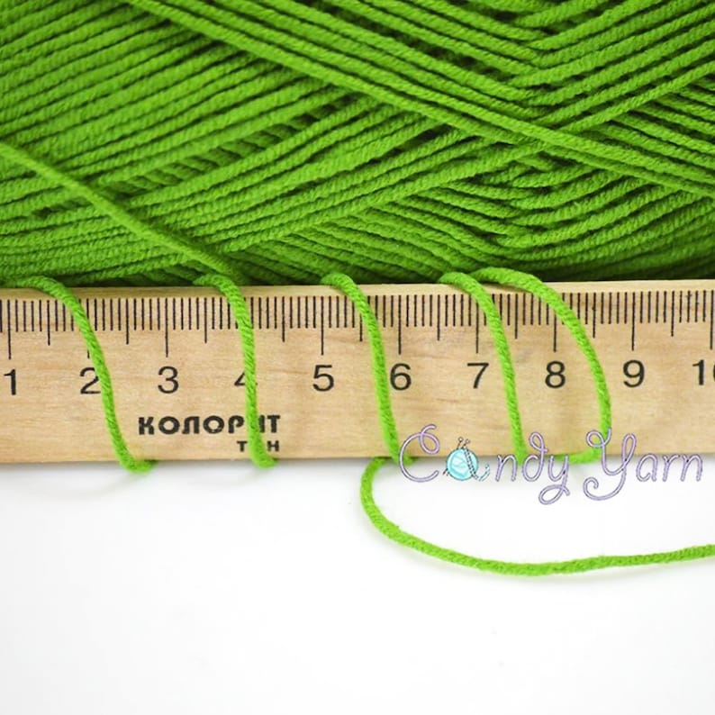 Puede incluir: Hilo verde brillante con una regla de madera que muestra medidas en cent&iacute;metros. El hilo es de color s&oacute;lido y la regla est&aacute; marcada con n&uacute;meros y texto. La imagen tambi&eacute;n incluye el texto "Candy Yarn".