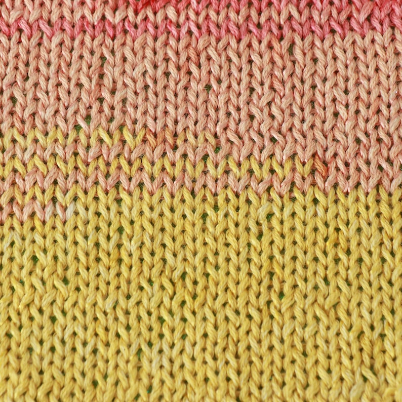 May include: Close-up of a knitted fabric with a gradient of pink and yellow colors. The fabric is made of a soft, textured yarn.