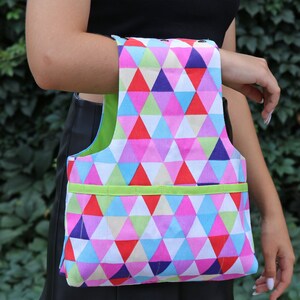 May include: A colorful tote bag with a geometric pattern of pink, blue, green, and red triangles. The bag has a green handle and a green trim around the top.