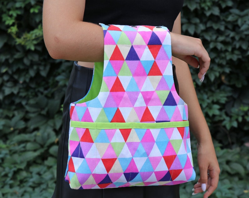 May include: A colorful tote bag with a geometric pattern of pink, blue, green, and red triangles. The bag has a green handle and a green trim around the top.