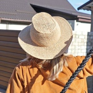 May include: A person wearing a wide-brimmed straw hat with a high crown, a brown corduroy jacket, and a black braided leather whip.