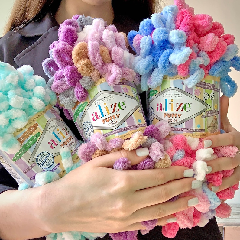 May include: Three spools of Alize Puffy Color yarn in pastel shades of pink, blue, and purple. The yarn is a looped chenille style, perfect for no-needle knitting projects. The labels read "Alize Puffy Color" and include the text "No Needles - No Hooks!"
