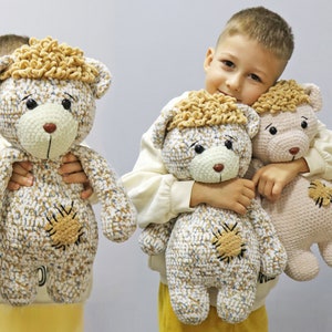 Könnte beinhalten: Ein Kind hält zwei gehäkelte Teddybären. Ein Bär ist braun und weiß mit einem braunen Fleck auf der Brust. Der andere Bär ist beige mit einem braunen Fleck auf der Brust. Beide Bären haben braune Augen und eine braune Nase.