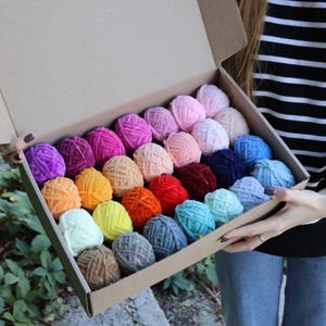 May include: A box filled with colourful yarn balls. The yarn is soft and fluffy, and the colours are bright and vibrant. The box is open, and the yarn is spilling out.
