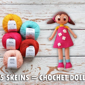 May include: A handmade crochet doll with a pink dress and white flower accents stands beside five skeins of colorful yarn. The yarn colors include yellow, teal, pink, red-orange, and peach. Text on the image reads "5 Skeins = Crochet Doll."