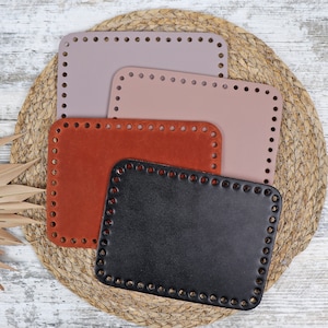 May include: Four leather bag straps in different sizes and colors. The straps are arranged in a stack, with the largest strap on the bottom and the smallest strap on top. The straps are made of brown, orange, pink, and black leather.