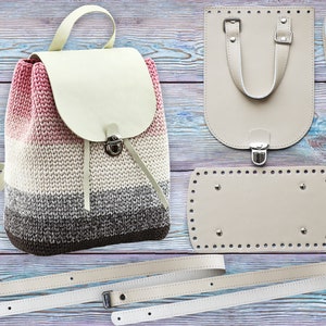 May include: A handmade backpack with a cream-colored flap and straps, and a knitted body in shades of pink, white, gray, and brown. The image also shows the components of a bag, including a base, a top piece, and straps.