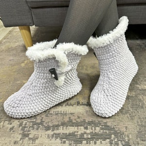 May include: Gray fuzzy slipper boots with a white faux fur trim and a black button closure.