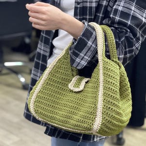 May include: A green crocheted tote bag with a white crocheted trim. The bag has a single strap and a unique crocheted detail on the front.