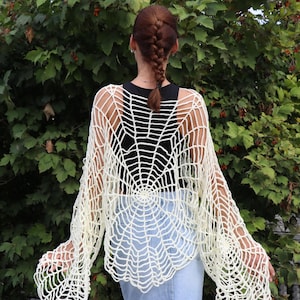 Könnte beinhalten: Ein weißes, gehäkeltes Oberteil in Form eines Spinnennetzes mit langen Ärmeln. Das Oberteil ist aus leichtem Garn gefertigt und hat eine lockere Passform.