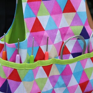 May include: A colorful, geometric patterned tote bag with multiple pockets for holding crochet hooks and yarn. The bag has a green trim and is made of a sturdy fabric.