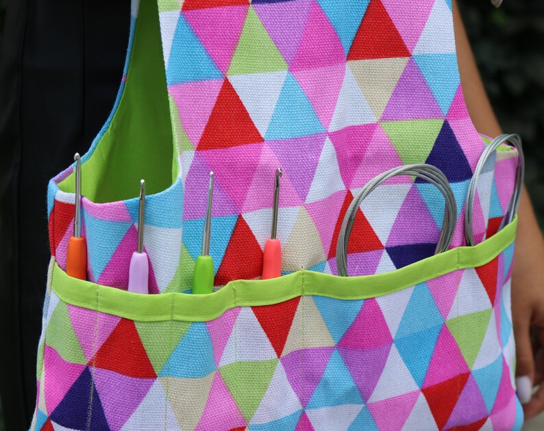 May include: A colorful, geometric patterned tote bag with multiple pockets for holding crochet hooks and yarn. The bag has a green trim and is made of a sturdy fabric.