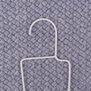 May include: White plastic hanger with a rounded top and a rectangular base. The hanger is on a gray textured surface.