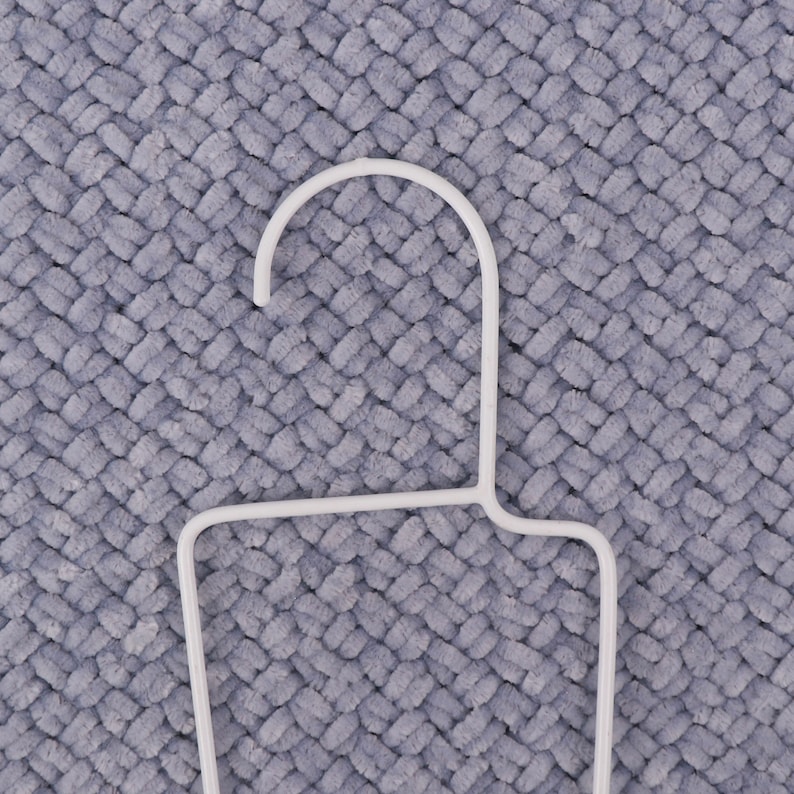 May include: White plastic hanger with a rounded top and a rectangular base. The hanger is on a gray textured surface.