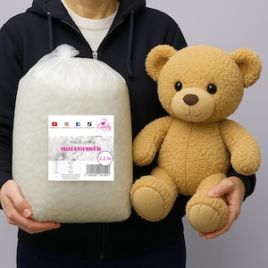 Könnte beinhalten: Ein Beutel mit "Hollfiber" Faserfüllung und ein Teddybär. Der Beutel ist transparent und zeigt die weiße Füllung, der Bär ist hellbraun. Der Beutel ist mit 1 kg gekennzeichnet. Der Bär wird neben dem Beutel gehalten.