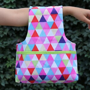May include: A colorful tote bag with a geometric pattern of pink, blue, red, and green triangles. The bag has a green ribbon across the top.