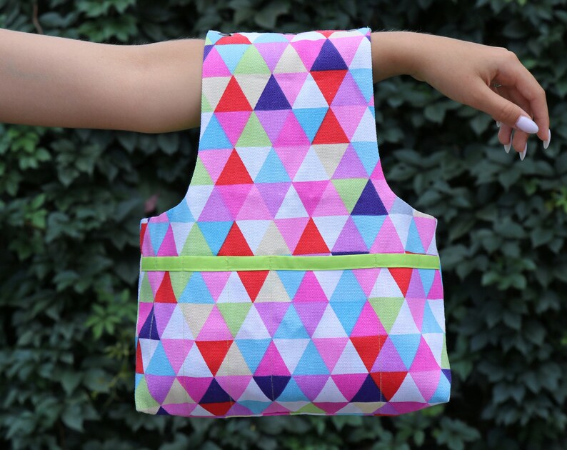 May include: A colorful tote bag with a geometric pattern of pink, blue, red, and green triangles. The bag has a green ribbon across the top.
