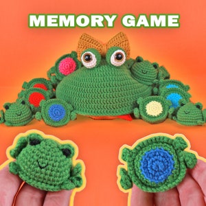 May include: A handmade crochet memory game featuring a large green frog with a bow and multiple smaller frog-shaped game pieces. The game pieces have different colored centers, including pink, blue, and yellow. The text "MEMORY GAME" is at the top.