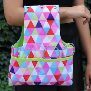 May include: A colorful, geometric patterned tote bag with a green lining and multiple pockets. The bag is filled with knitting needles and circular needles.