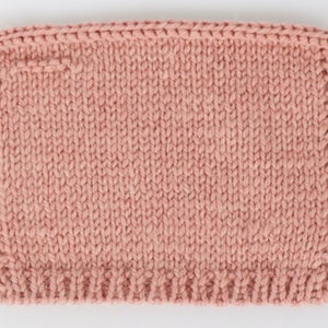 May include: A close-up of a knitted fabric in a dusty rose color. The fabric is knit in a simple stitch, creating a smooth and even texture.