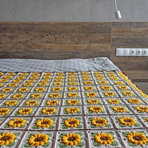 K&ouml;nnte beinhalten: Eine handgefertigte H&auml;keldecke mit einem sich wiederholenden Sonnenblumenmuster. Die Decke besteht aus gelber, brauner, gr&uuml;ner und wei&szlig;er Wolle. Die Decke liegt auf einem Bett mit einem h&ouml;lzernen Kopfteil.
