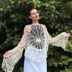 Può includere: Un top bianco all'uncinetto con un design a ragnatela. Il top ha maniche lunghe e una vestibilità ampia.