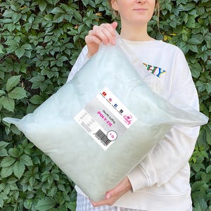 May include: A clear plastic bag filled with fiberfill stuffing. The bag has a label that reads "POLY-FIL" and "fiberfill stuffing". The label also includes the weight, 1 lb. The bag is held in front of a green leafy background.