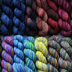 May include: A collection of colorful yarn skeins in various shades of blue, green, red, yellow, and orange. The yarn is arranged in two rows, with the top row featuring solid colors and the bottom row featuring multi-colored skeins.