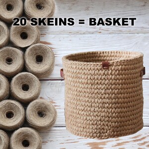 K&ouml;nnte beinhalten: Ein brauner geh&auml;kelter Korb mit Ledergriffen. Der Korb ist aus 20 Kn&auml;uel Garn gefertigt und steht auf einer wei&szlig;en Holzoberfl&auml;che. Der Text "20 SKEINS = BASKET" ist in schwarzen Buchstaben auf wei&szlig;em Hintergrund geschrieben.