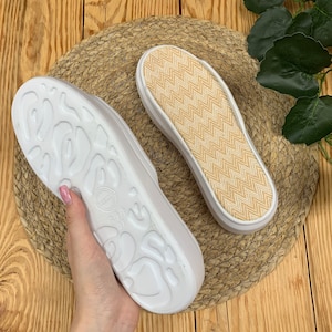 May include: A pair of white canvas slip-on shoes with a textured sole. One shoe has a beige chevron pattern on the insole.